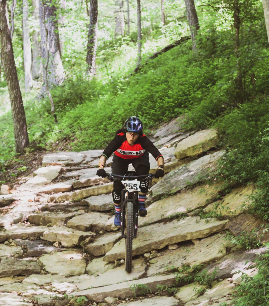 Female racer riding downhill on large rocks.