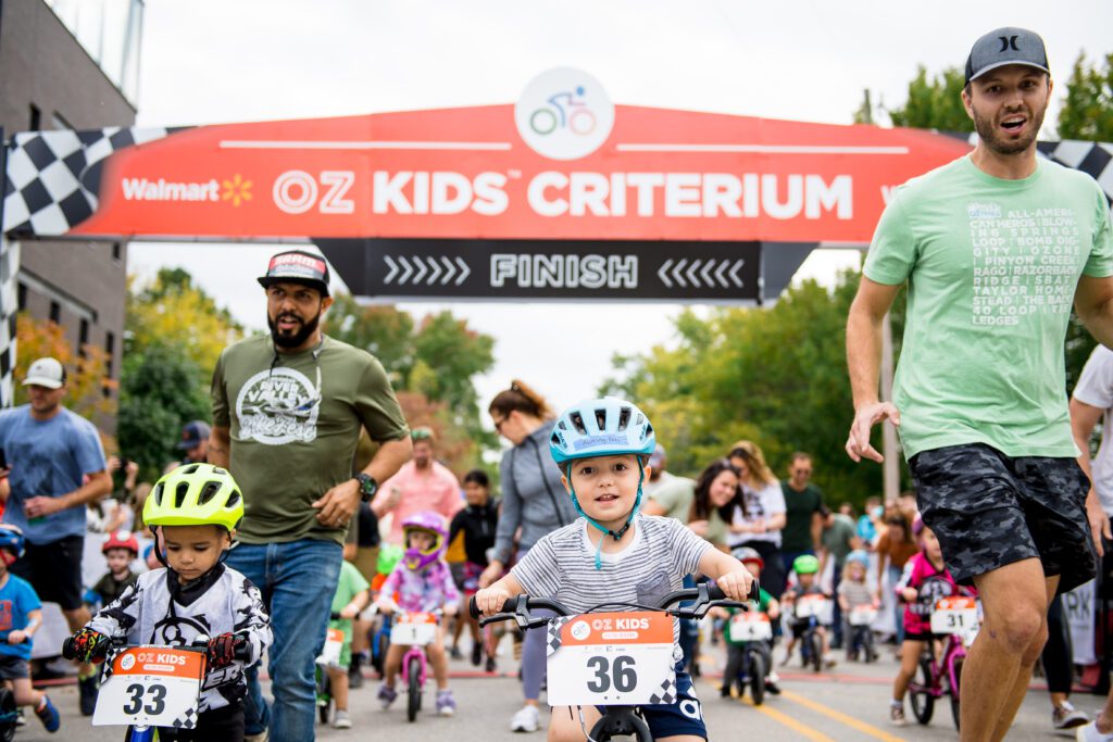 Young children race their bike with parents running alongside them.