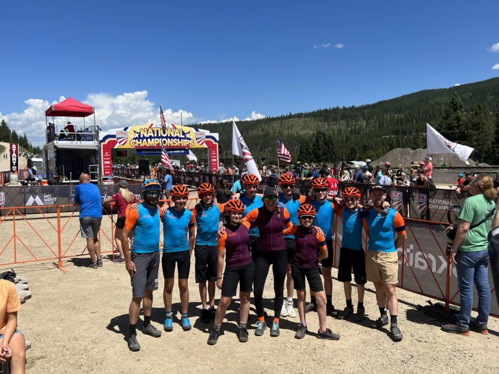 Group of teenagers stand in front of the "National Championship" banner at a bike race.