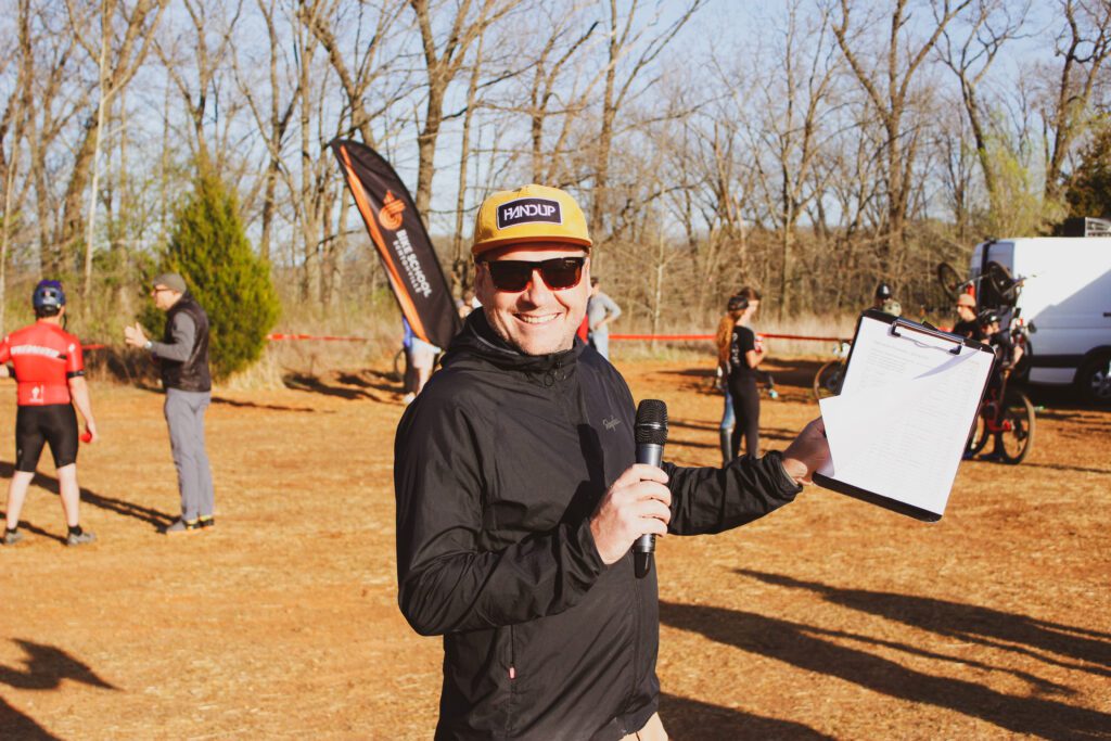 Race commentator holding a microphone and score sheet.