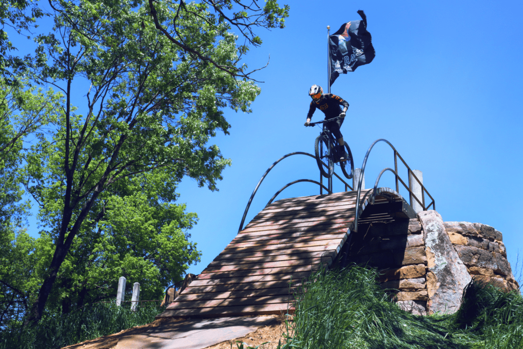 Rider going down a roll in feature with an OZ trails flag waving in the background