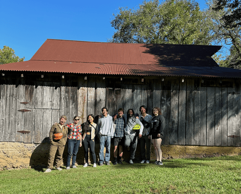 A group poses in front of a brown barn for a photo.