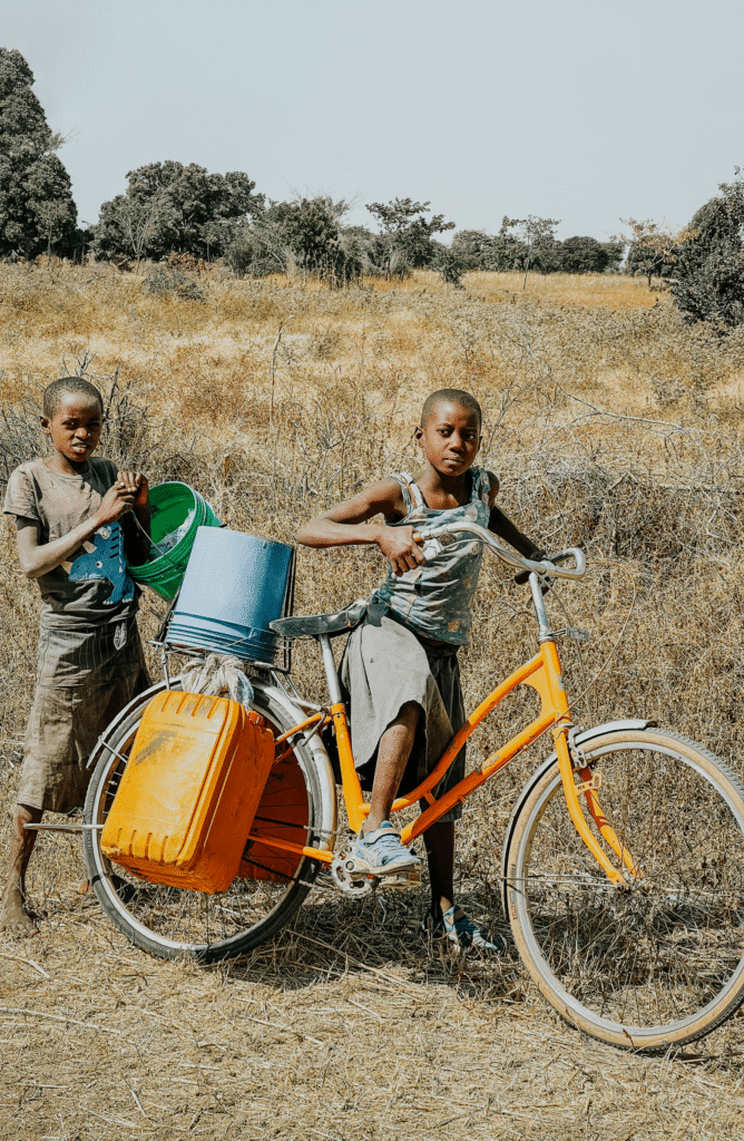 Two children in Tanzania use a bike to transport water.